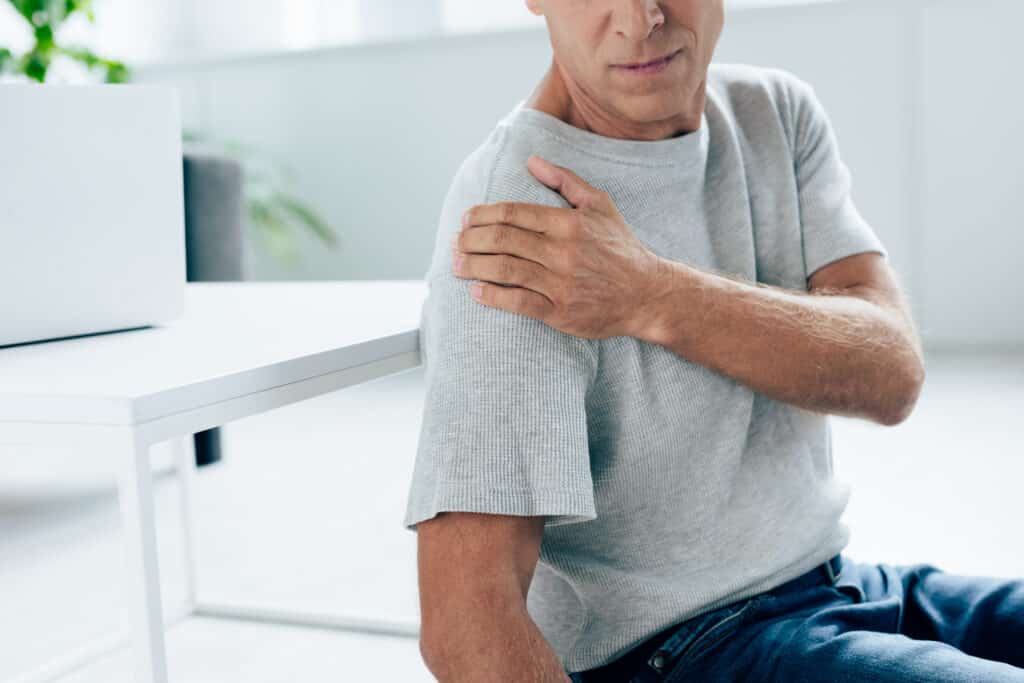 cropped view of man in t shirt feeling pain in shoulder in apartment